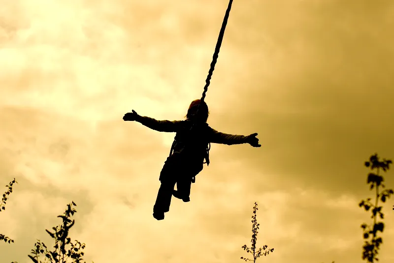 Silhouette of a bungee jumper against a golden sunset sky