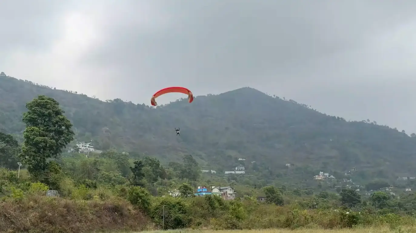 Single paraglider over the green valley and hills of Bhimtal