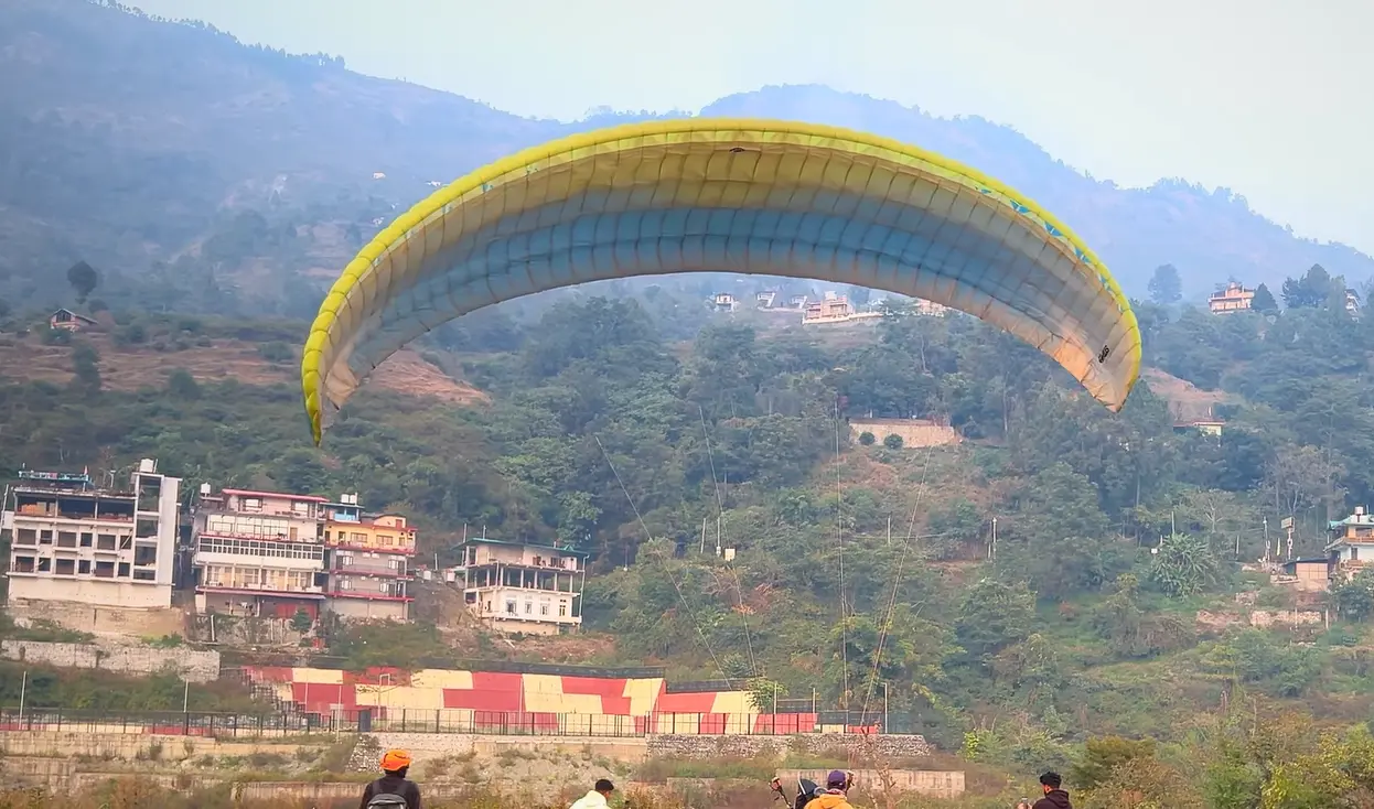 Paraglider coming in to land over the hill town near Bhimtal