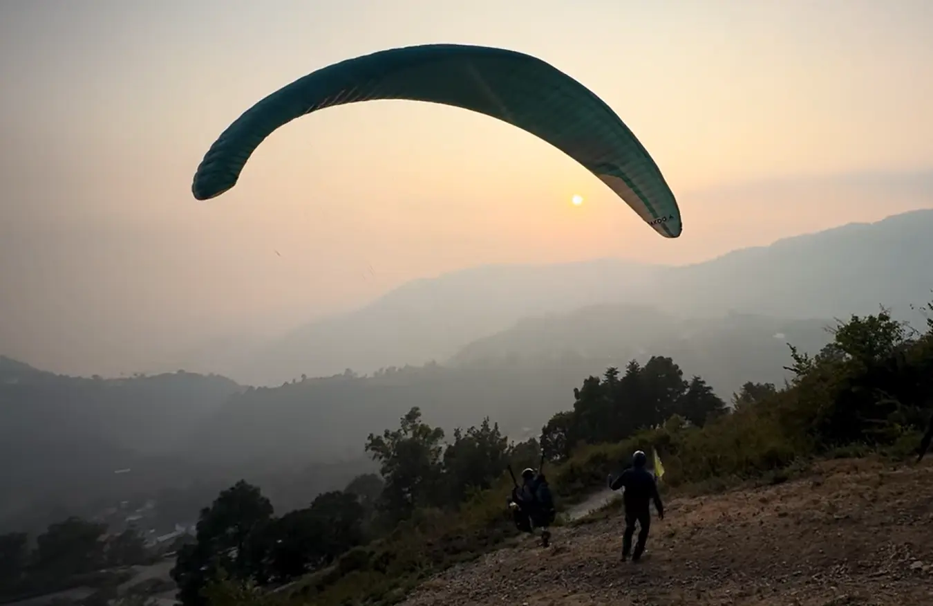 Paraglider against a sunset sky above the hills near Bhimtal