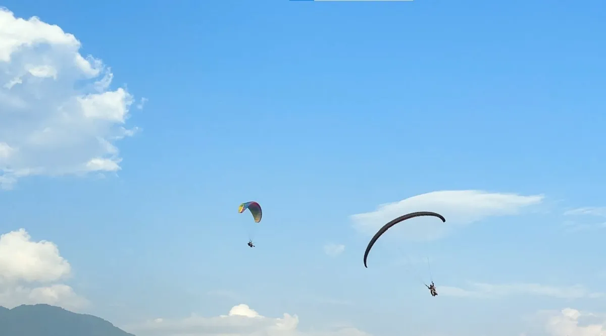 Tandem paraglider flying above the hills with the pilot and passenger in the harness