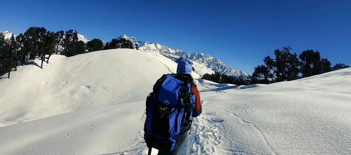 trekker with a backpack walking through deep snow on the Brahmatal trek, with snow peaks ahead