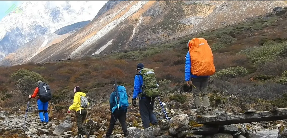 group of trekkers with backpacks crossing rocky ground below snow-dusted slopes on the Goechala trek