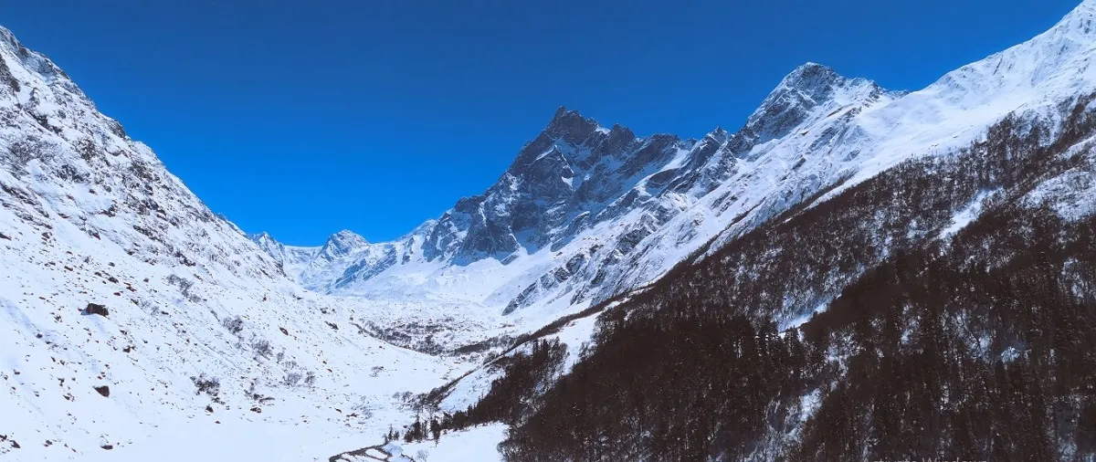 snow-covered Har Ki Dun valley below a sharp rocky peak under a blue sky