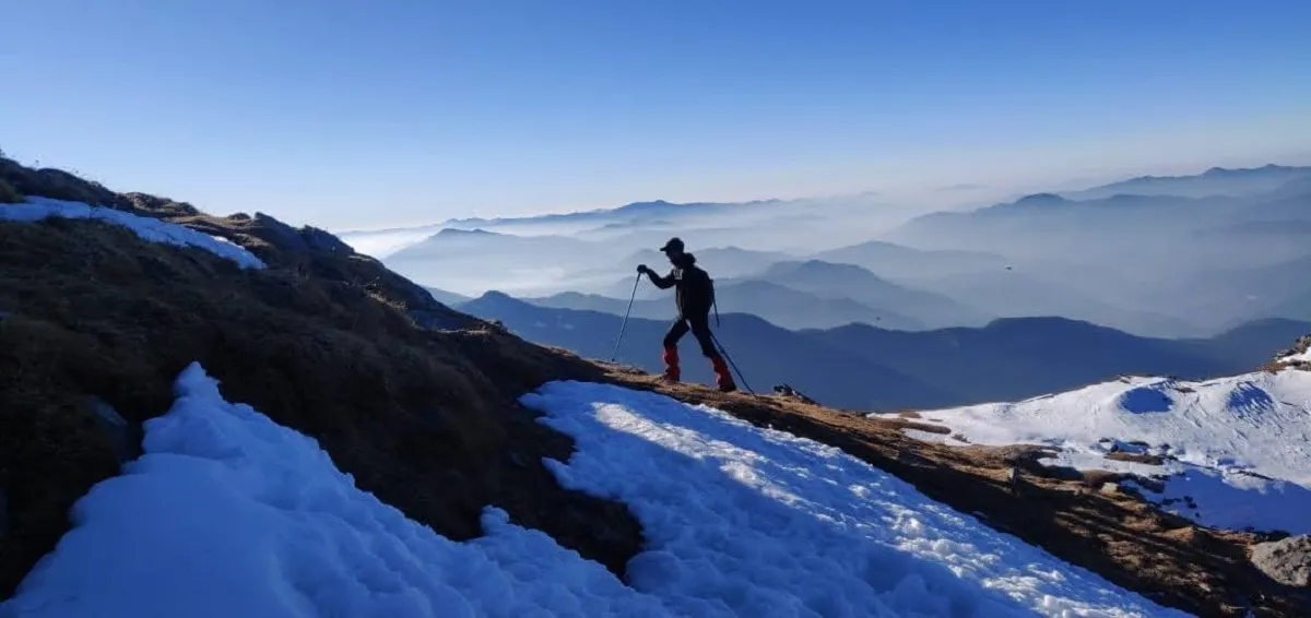 trekker climbing a snowy ridge on the Kedarkantha trek above a sea of clouds
