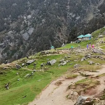 Green Triund meadow and trail with forested hills