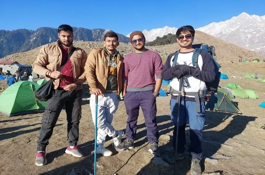Trekkers at the Triund campsite with tents and the snowy Dhauladhar range behind