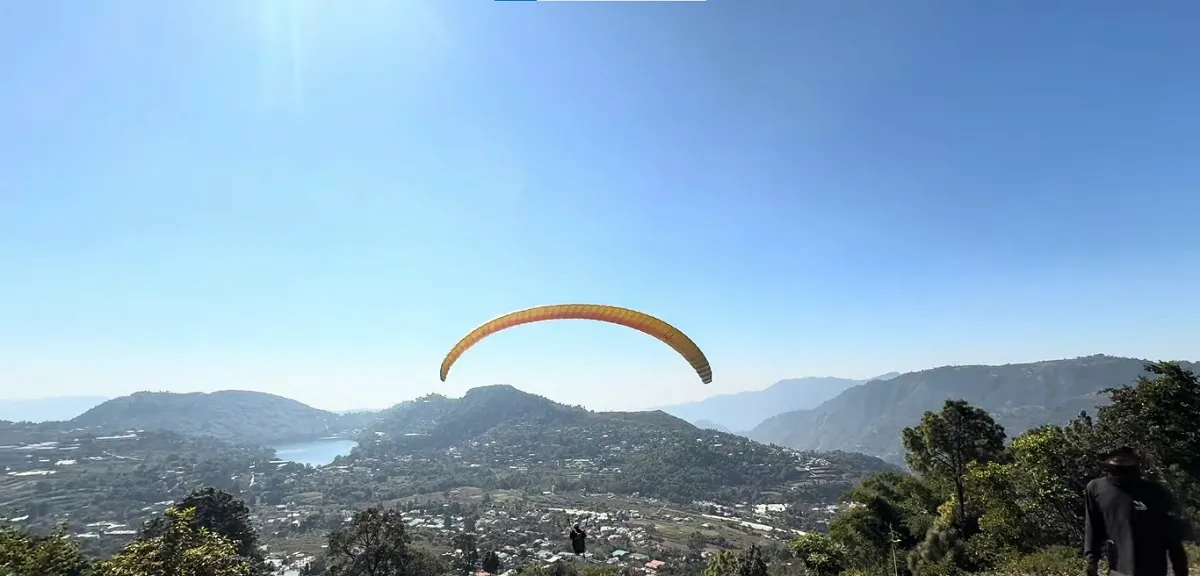 Tandem paraglider flying over the hills near Bhimtal with a lake in the valley below