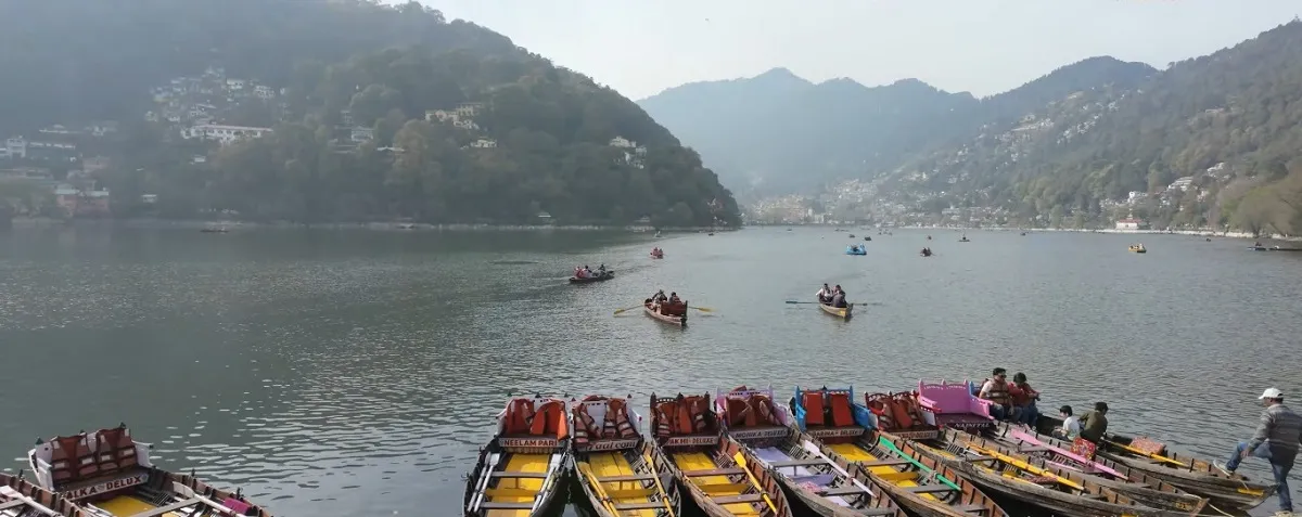 Colourful rowing boats lined up at the Naini Lake boat stand, with boaters out on the lake