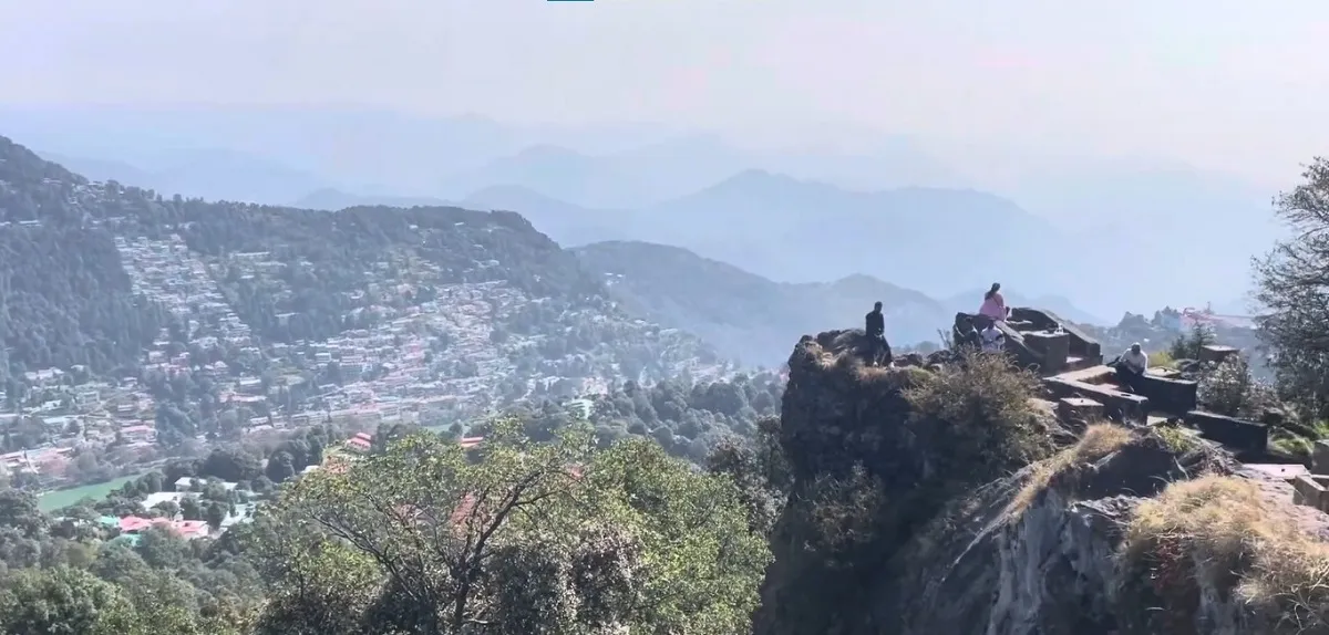 Visitors on the rocky viewpoint at Tiffin Top above Nainital, with the town and hills below