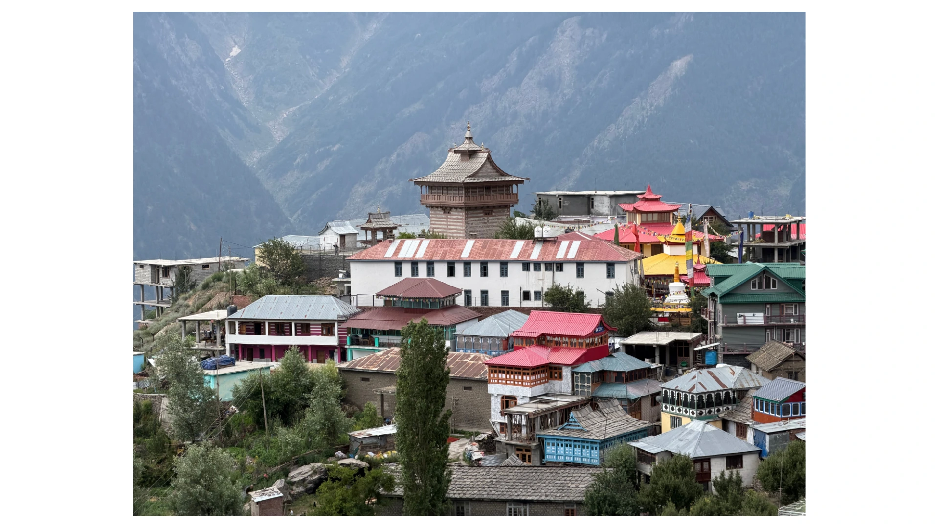 Village in the Kinnaur Valley with a wooden tower, colourful houses and a Buddhist stupa below snowy hills