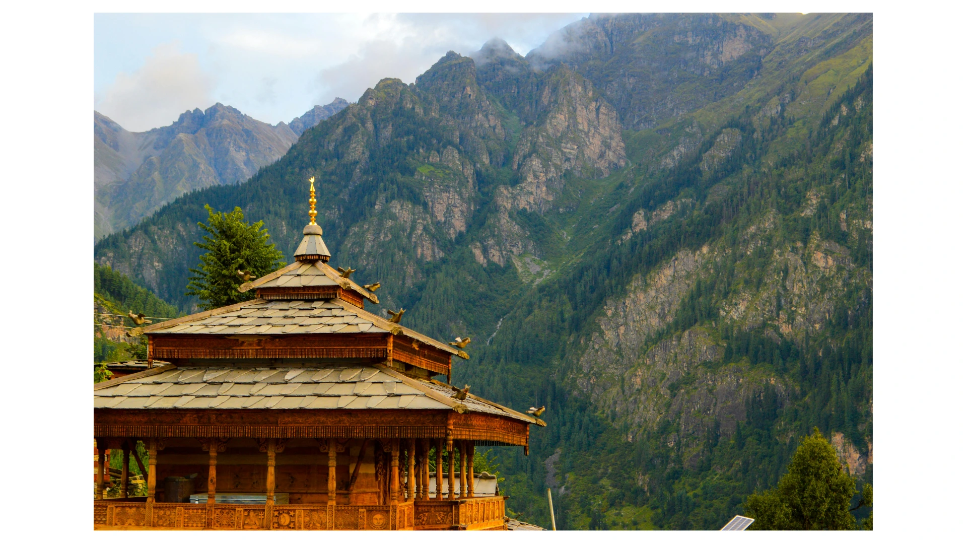 Wooden temple roof with carved birds and forested mountains in the Baspa Valley