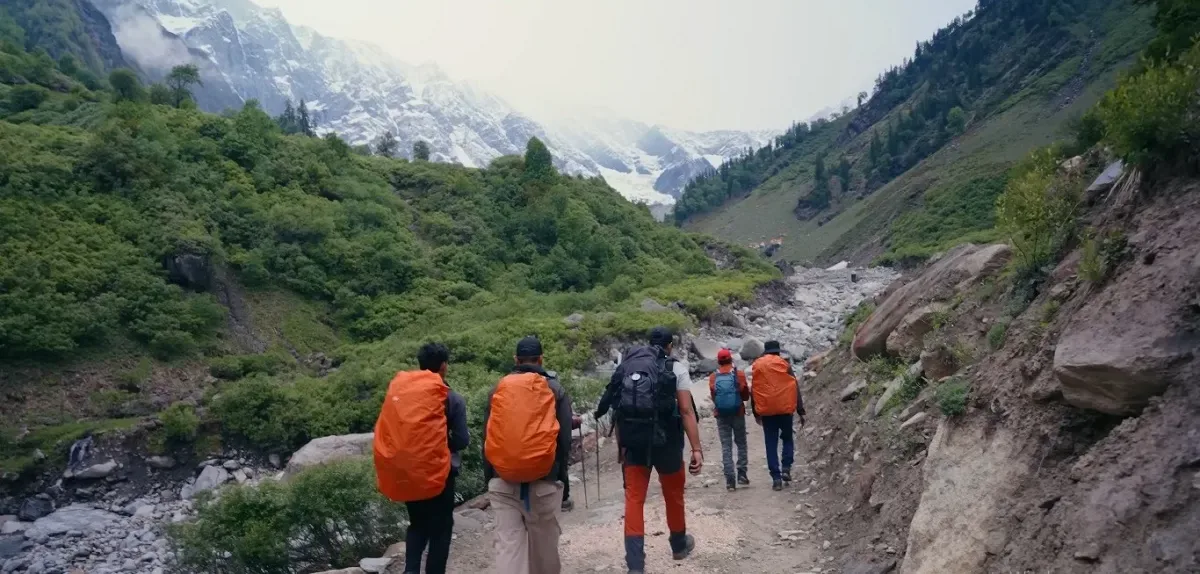 Trail through the valley on the Friendship Peak trek Trekkers with orange rain covers walking a rocky trail through a green Himalayan valley below snow peaks on the Friendship Peak trek