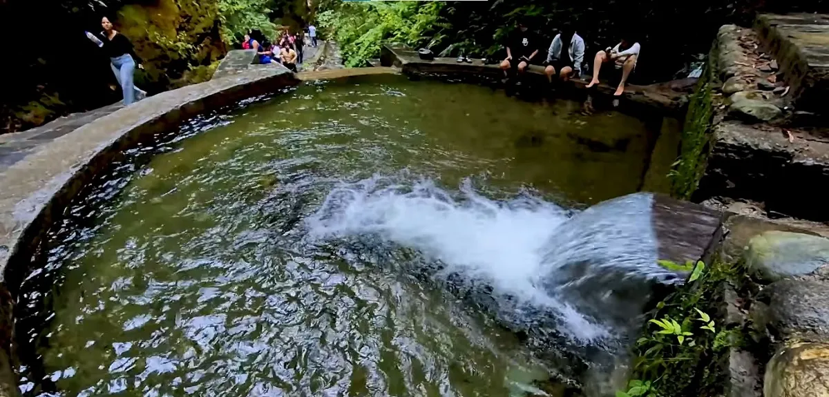 Water falling into a stone pool surrounded by rocks and greenery