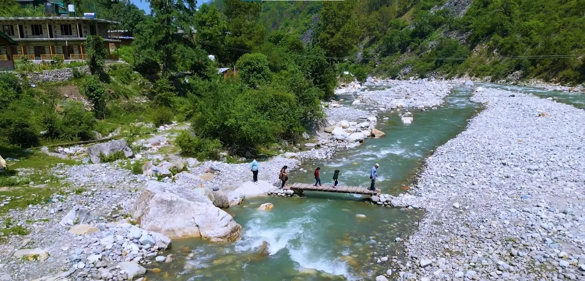 Tirthan river with a wooden footbridge crossing the clear water