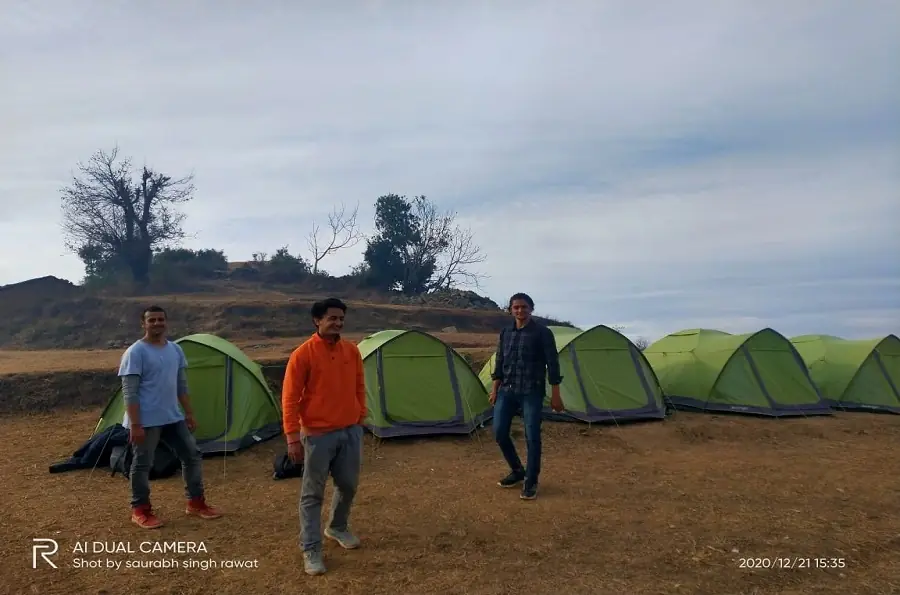 Trekkers beside green tents at Nag Tibba base camp on a clear December afternoon before the snowfall