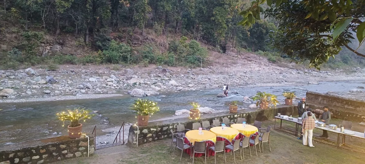 Dining tables set up on a lawn beside the river at a camp near Rishikesh