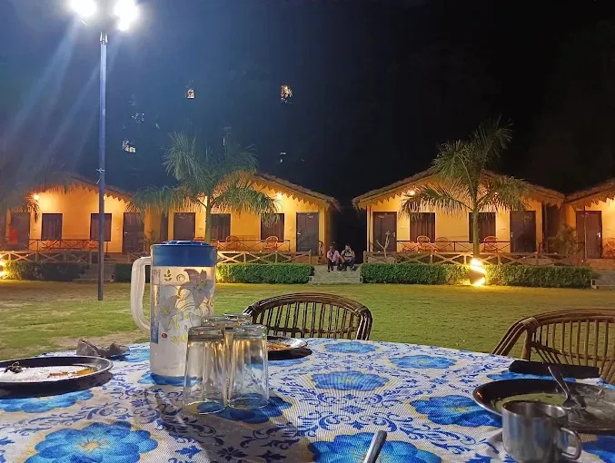 Cottages and lawn at Nakshatra Resort on Neelkanth Road, Rishikesh, lit up at night, with a dinner table in front