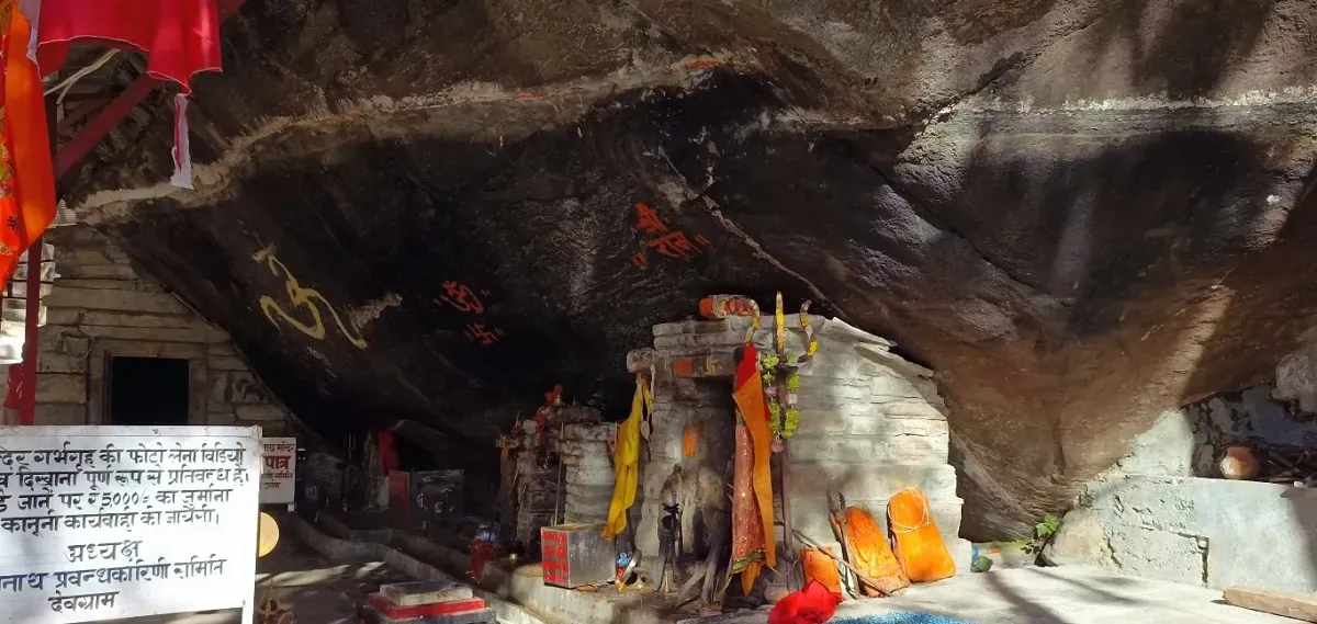 Kalpeshwar cave temple under an overhanging rock, decorated with flags and offerings
