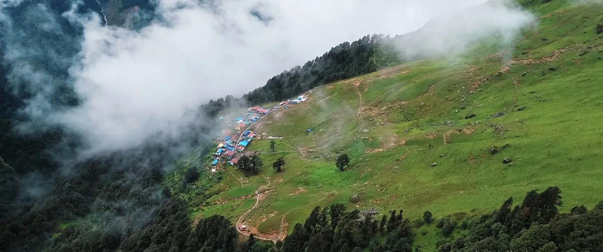 Tents on a green Himalayan meadow on the Madhyamaheshwar trek, with clouds rolling over the forest