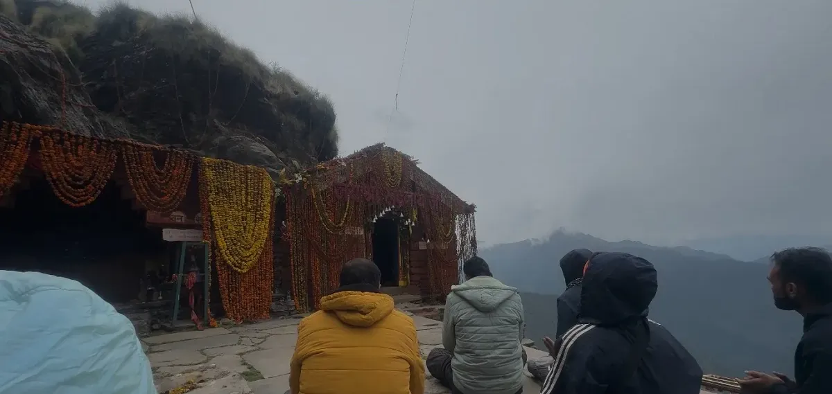 Pilgrims in rain jackets resting outside Rudranath Temple on a misty day