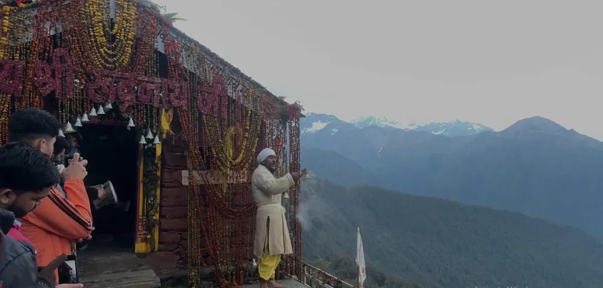 Priest performing aarti at the garlanded Rudranath Temple, the fourth Panch Kedar shrine, with snow-capped Himalayan peaks behind