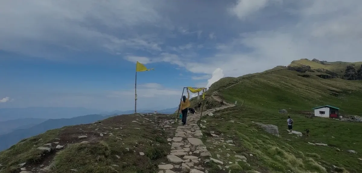 Trekkers walking across steep grassy bugyal slopes and rocky ridges on the Rudranath trail